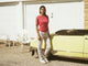 Mey Tweedelige Pyjama Dames 1240115 1700 strawberry glaze, roze shirt en bloemenpyjamabroek bij een gele auto.