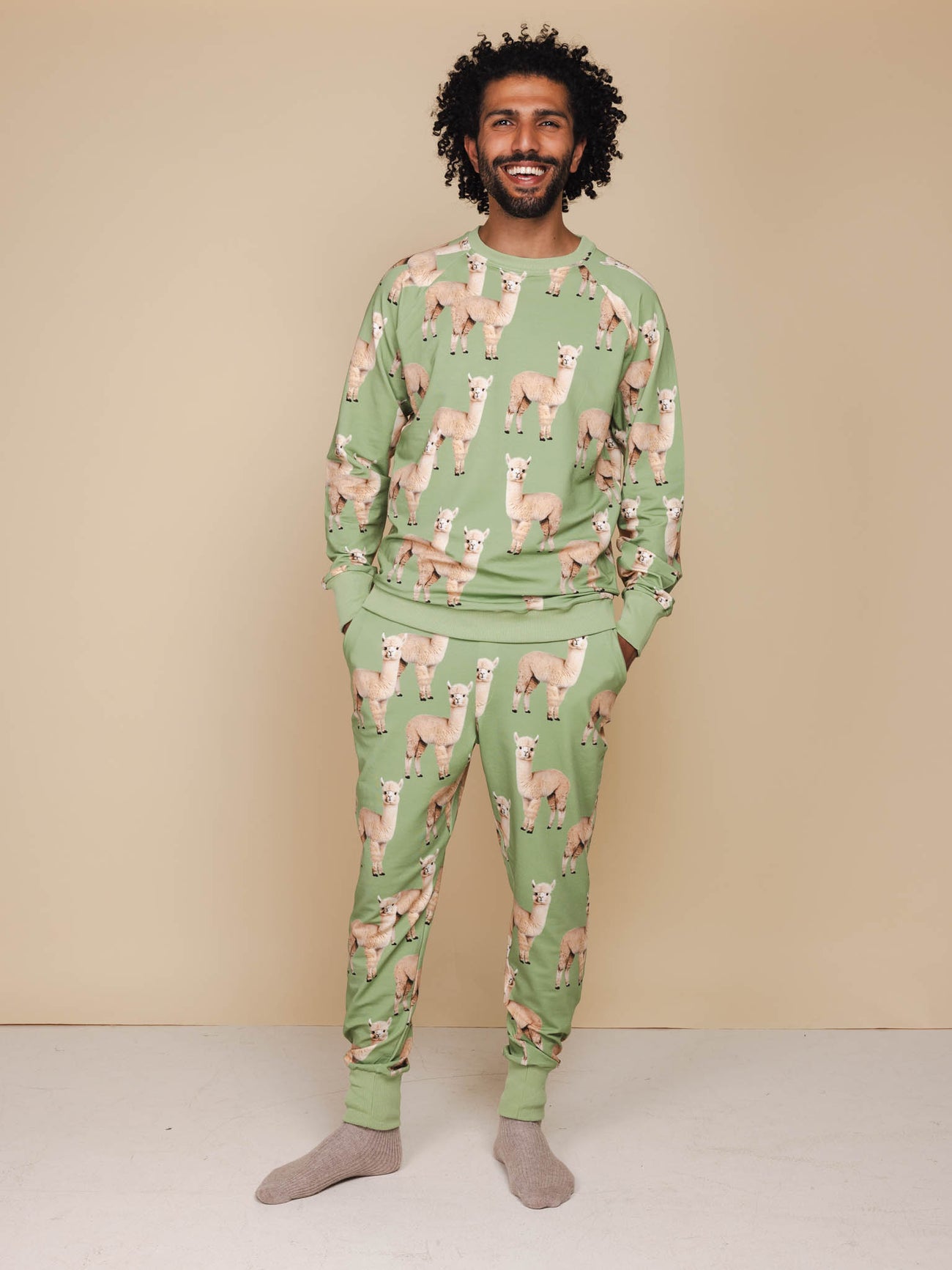 Snurk Alpaca Meadow Broek Unisex in een groene kleur met leuke alpacaprint, gedragen door een lachende man.