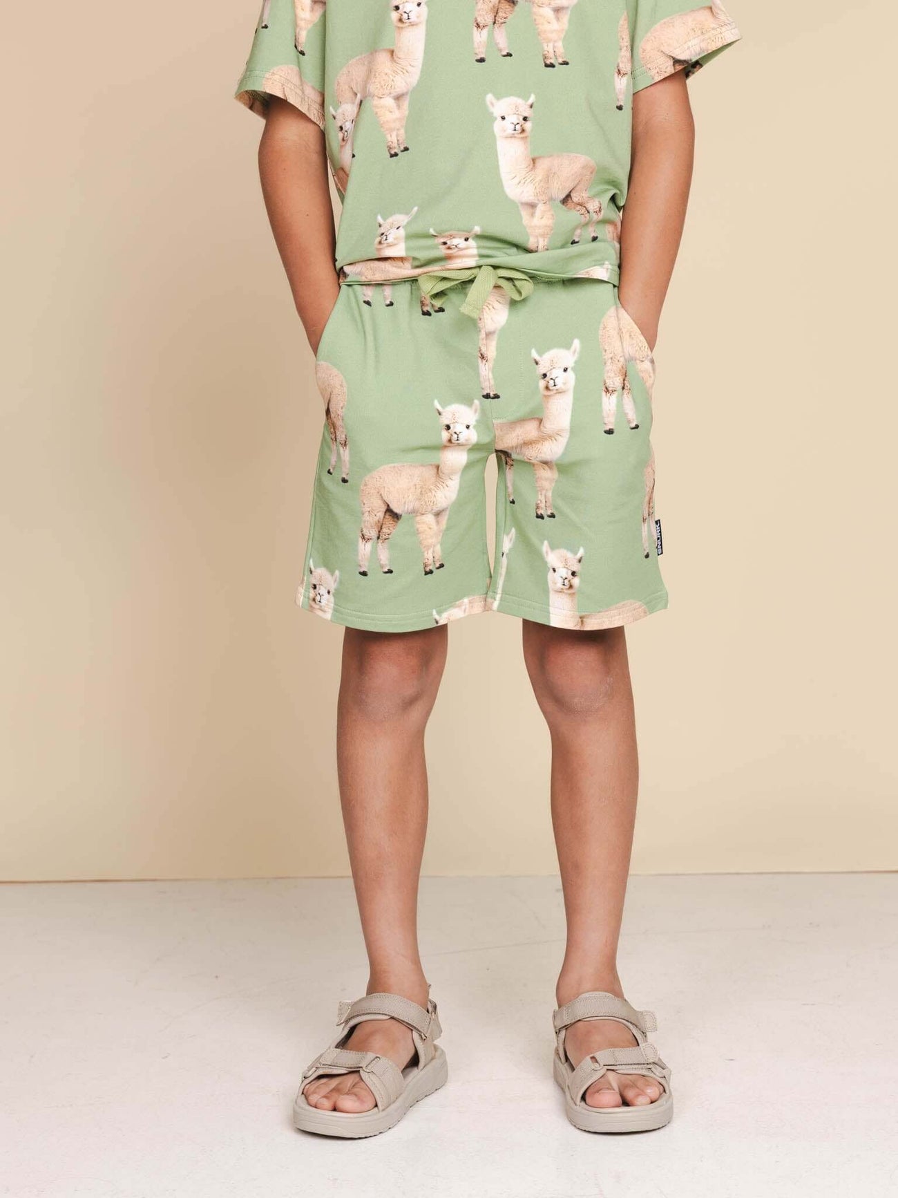Kind in SNURK Alpaca Meadow Shorts Kids met schattige Alpacaprint, ontspannen fit en gemaakt van biologische katoen.
