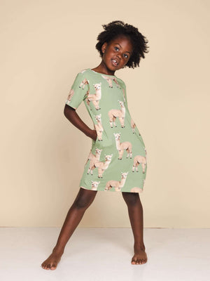 SNURK Alpaca Meadow T-shirt Dress Kids model in vrolijk jurkje met alpacaprint op een neutrale achtergrond.