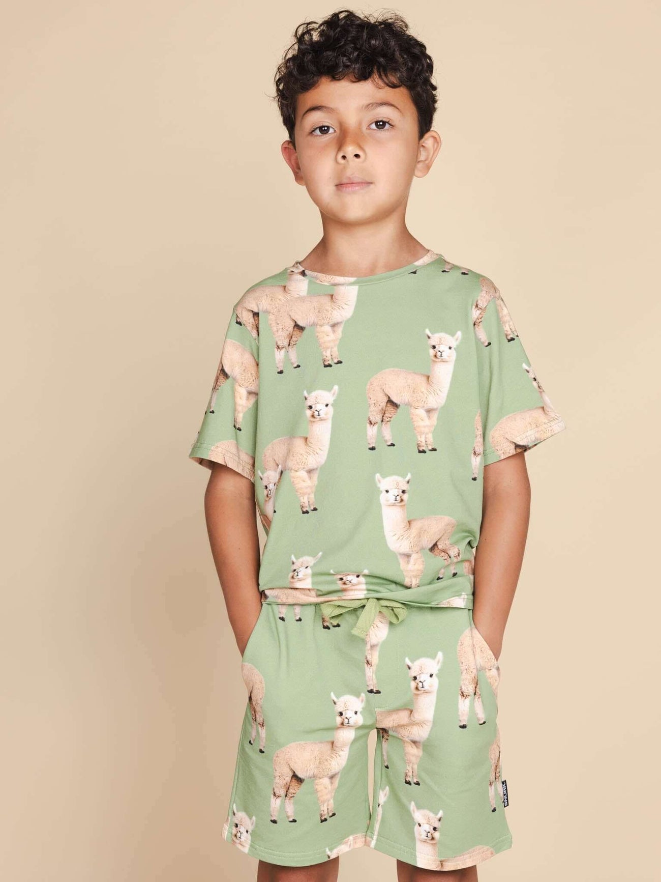 Jongen draagt SNURK Alpaca Meadow T-shirt Kids met alpacaprint op een beige achtergrond.