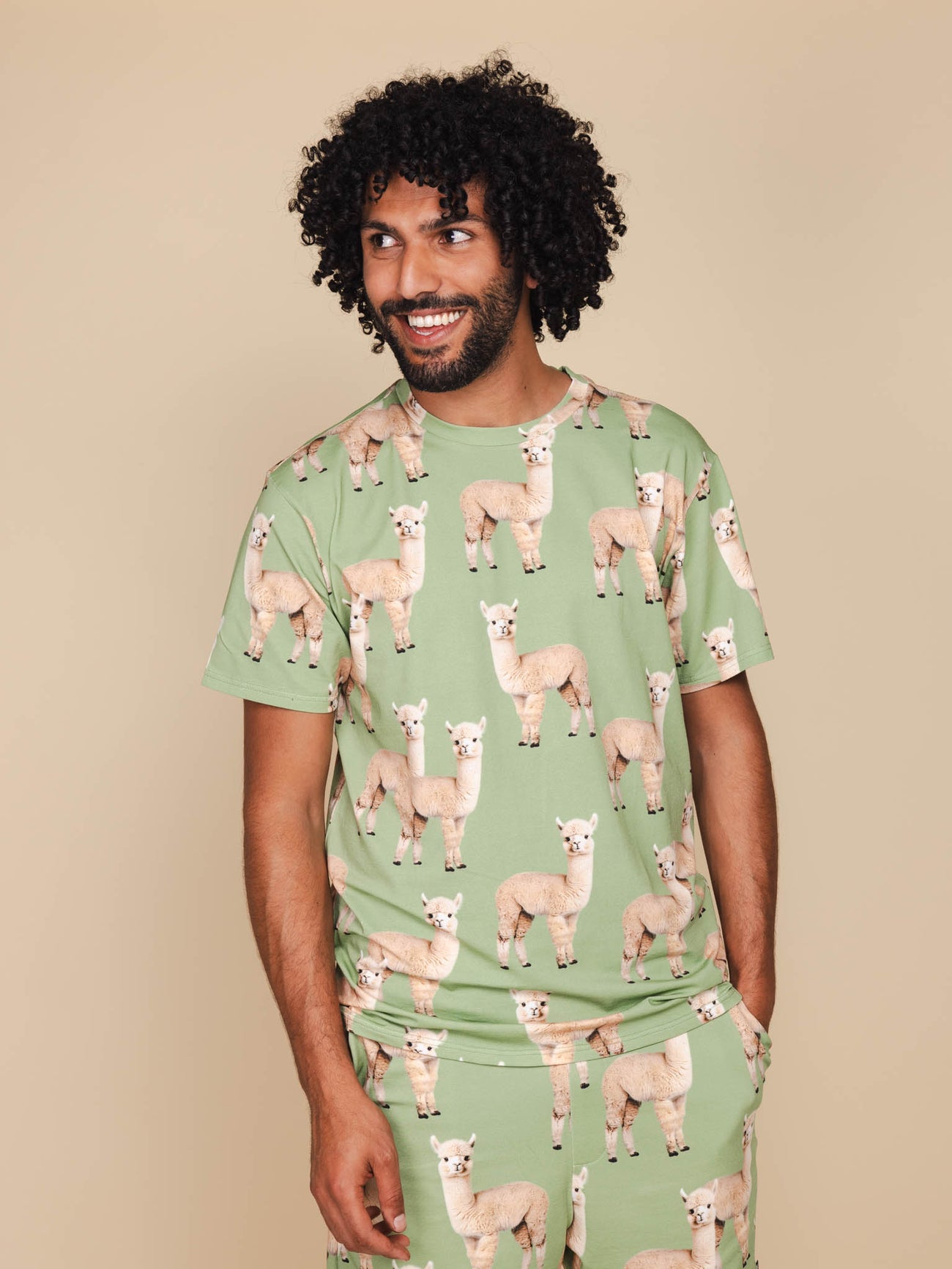 Man in SNURK Alpaca Meadow T-shirt Unisex met alpacaprint op een lichte achtergrond.