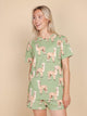 SNURK Alpaca Meadow T-shirt Unisex met alpacaprint gedragen door een vrouw op een beige achtergrond.