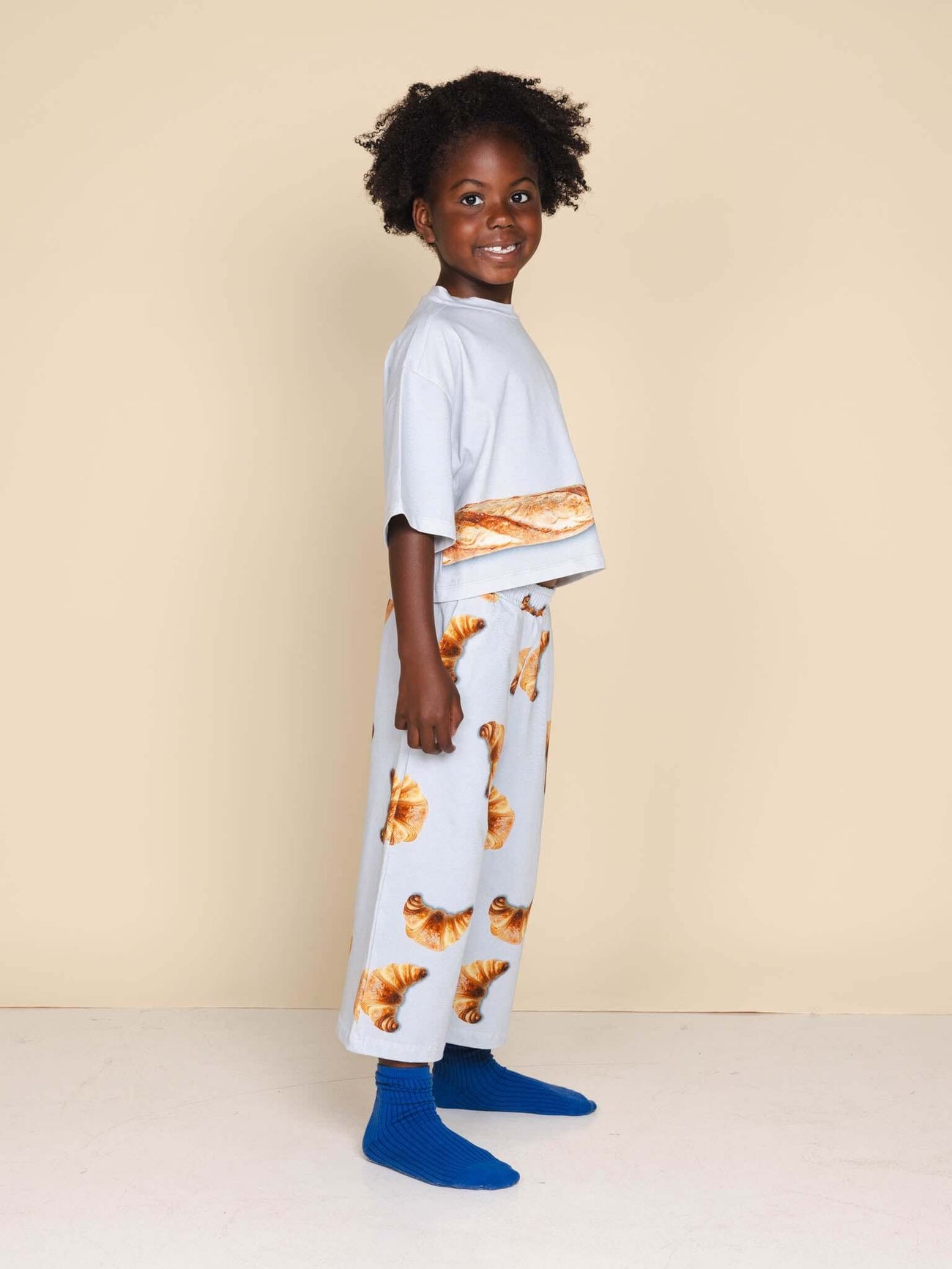 SNURK Baguette Cropped T-Shirt Kids, kind in pyjama met deegwaren print, ontspannen stijl, zachte stof, ideale nachtkleding.