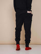 SNURK Black Broek Regular Unisex stijlvolle zwarte joggingbroek gezien van achteren met rode sokken.