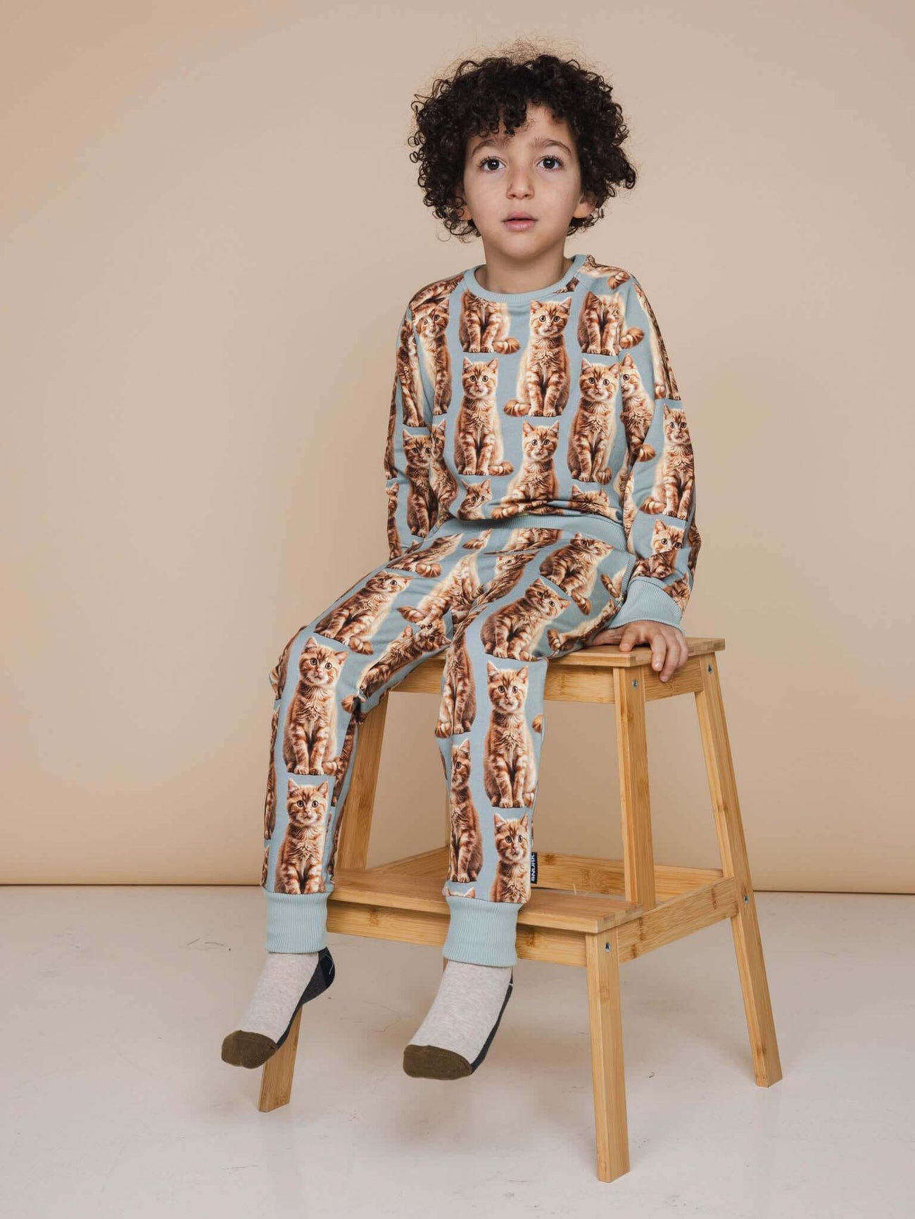 SNURK Bowie Broek Kids model met kattenprint zittend op een houten kruk in kinderkleding.
