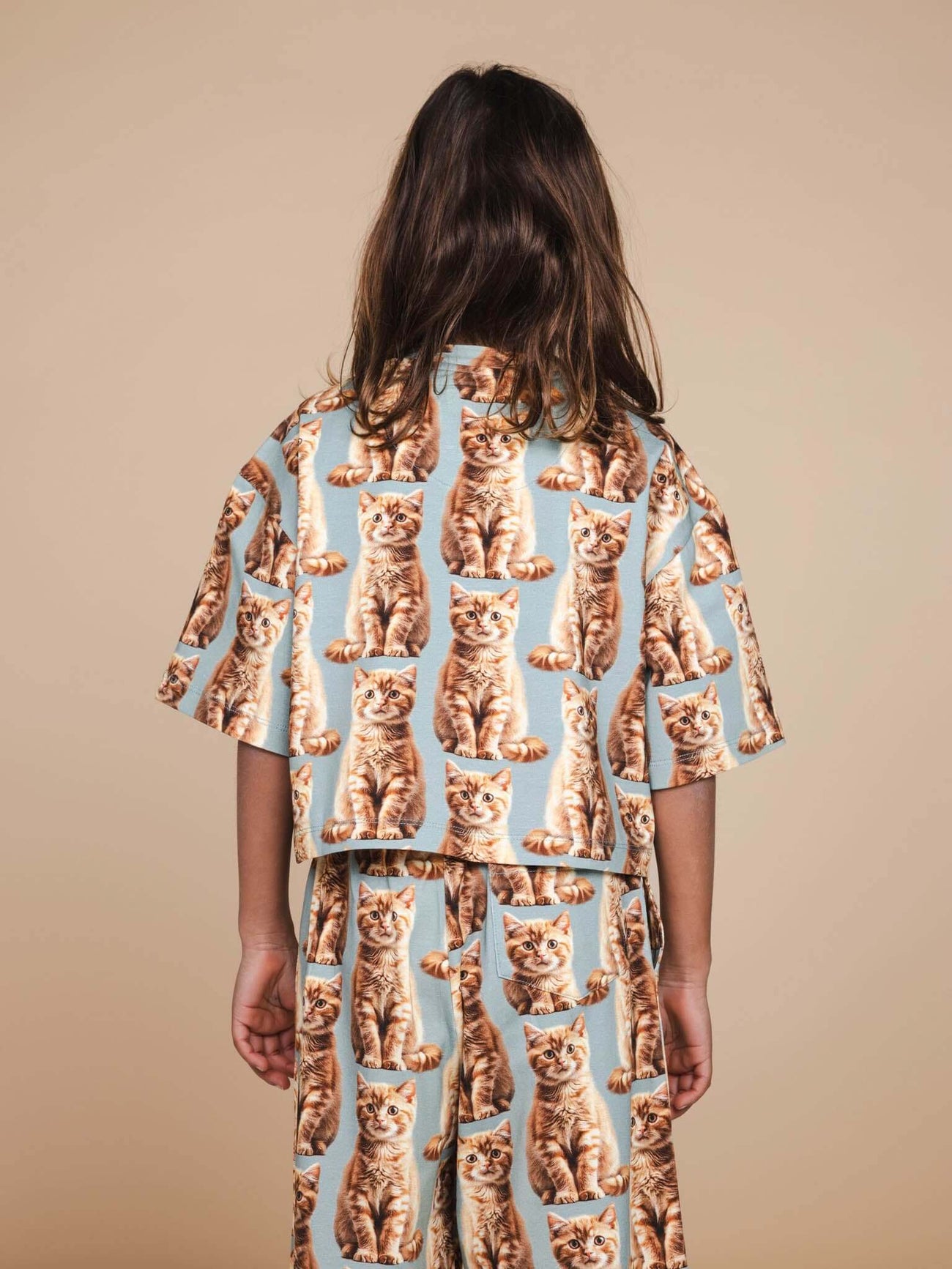 SNURK Bowie Cropped T-Shirt Kids met schattige katprint op een kind in een beige achtergrond.