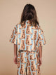 SNURK Bowie Cropped T-Shirt Kids met schattige katprint op een kind in een beige achtergrond.
