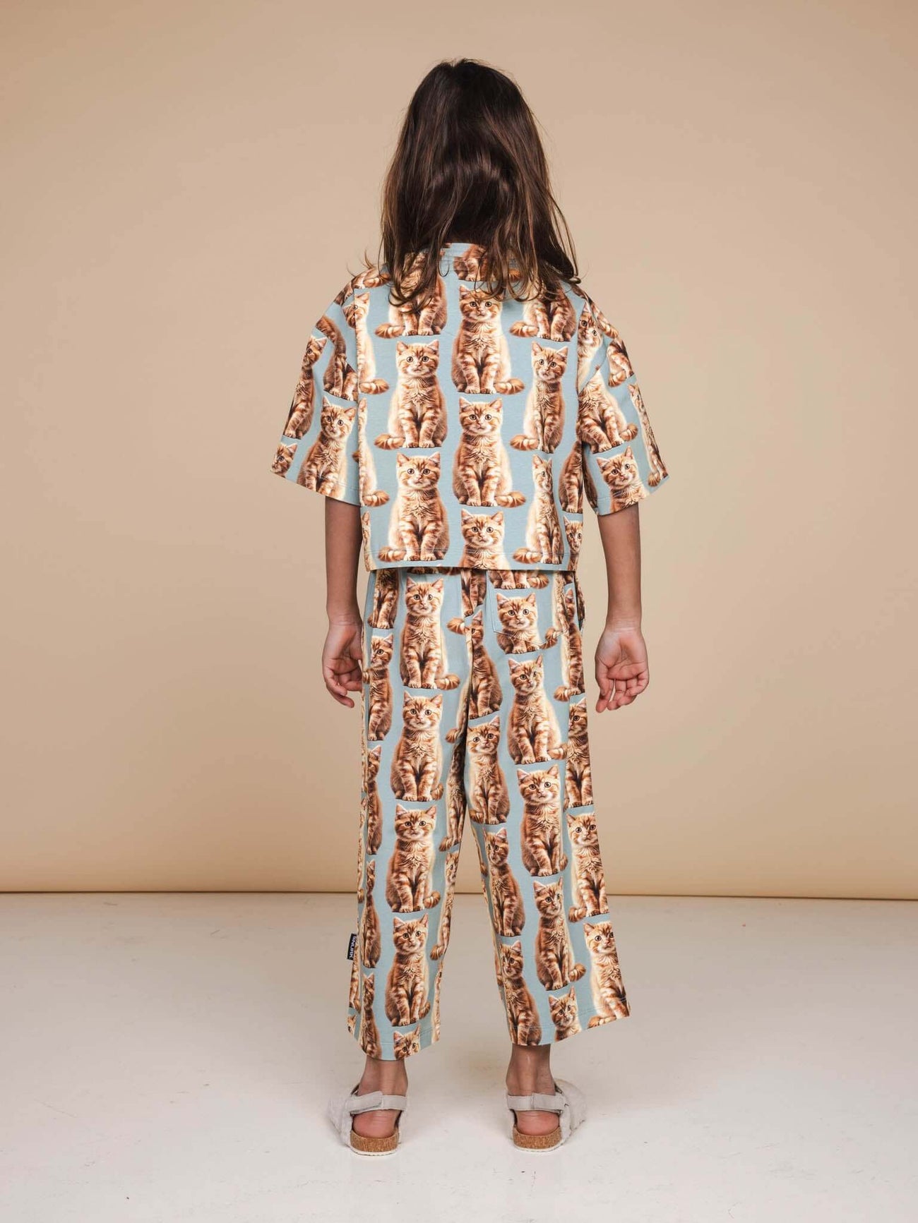 Kind in SNURK Bowie Cropped T-Shirt Kids met kattenprint, achterkant gezien op lichte achtergrond.
