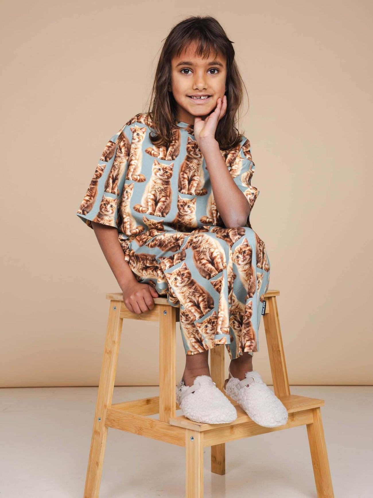 Kind in SNURK Bowie Cropped T-Shirt Kids met katjesprint, zittend op een stoel.