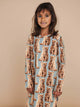 Meisje in SNURK Bowie Long Sleeve Dress Kids met schattige kattenprint en lange mouwen.