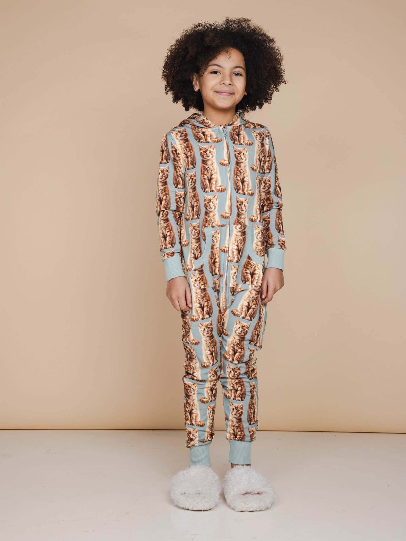 Een kind in een SNURK Bowie Onesie Kids met een schattige kattenprint, ideaal voor slaap- en spelplezier.