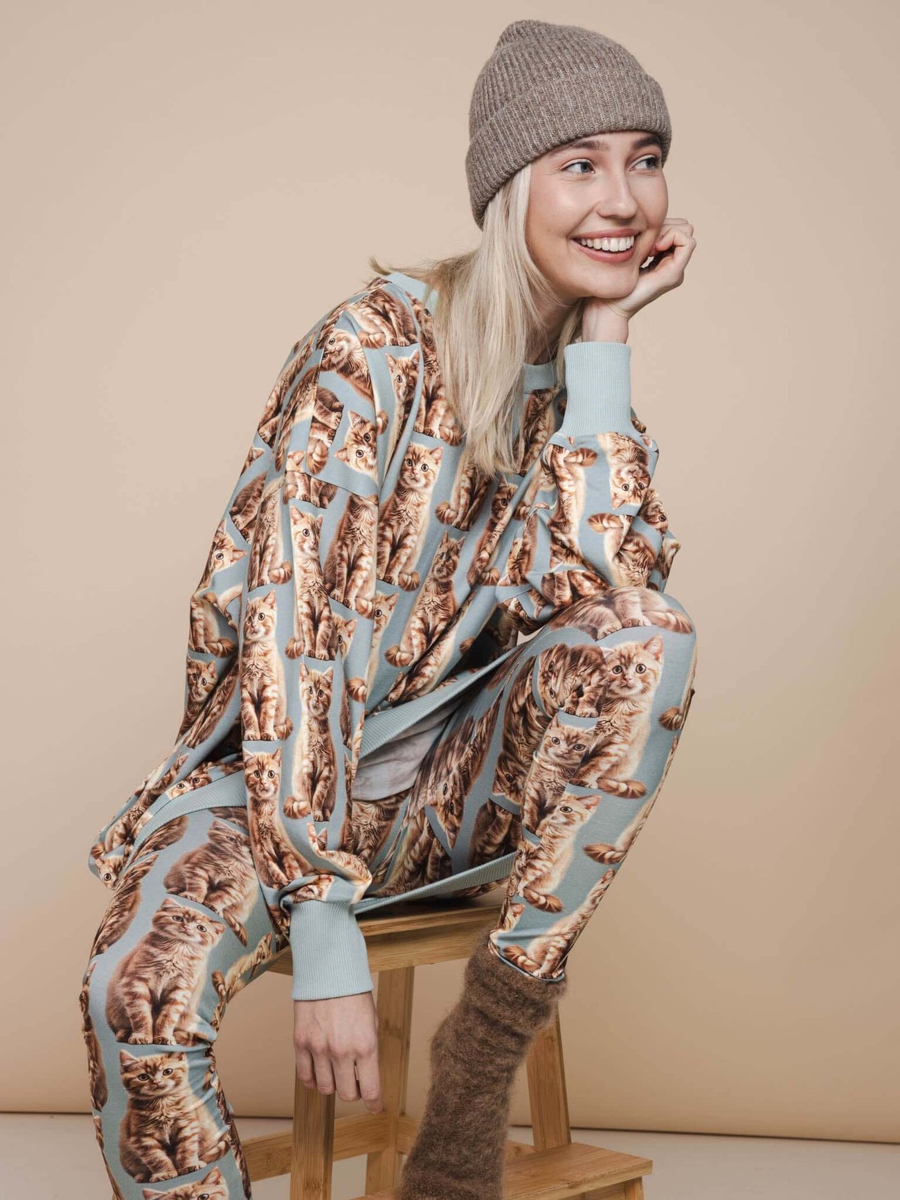 SNURK Bowie Sweater Dress Dames model met kattenprint, zittend op een stoel met een vrolijke uitstraling.