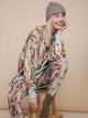 SNURK Bowie Sweater Dress Dames model met kattenprint, zittend op een stoel met een vrolijke uitstraling.