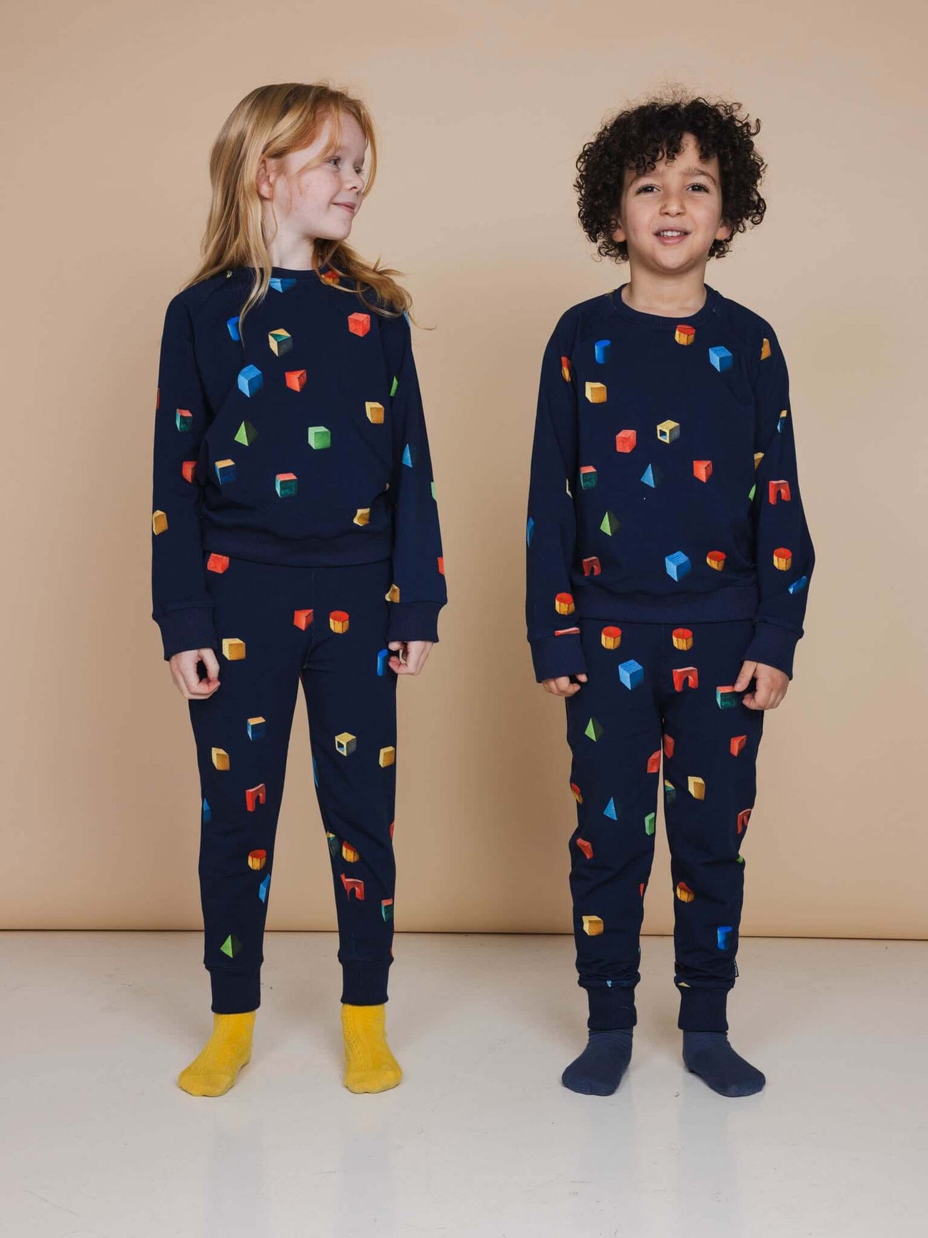 Kinderen in SNURK Building Blocks Broek Kids met kleurrijke blokken print op een donkerblauwe achtergrond.