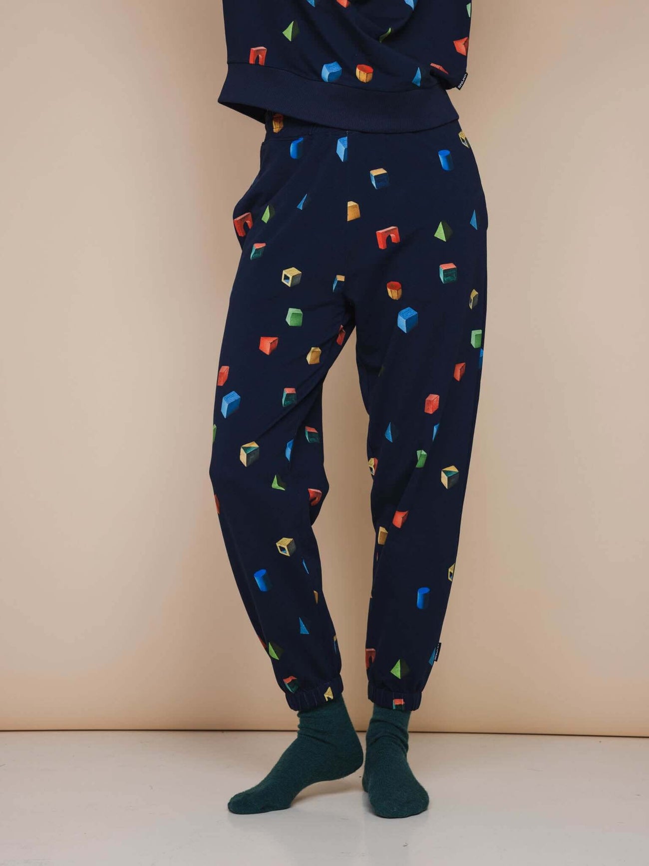 SNURK Building Blocks Broek Relaxed Unisex met kleurrijke houten blokken op een navy blauwe achtergrond.