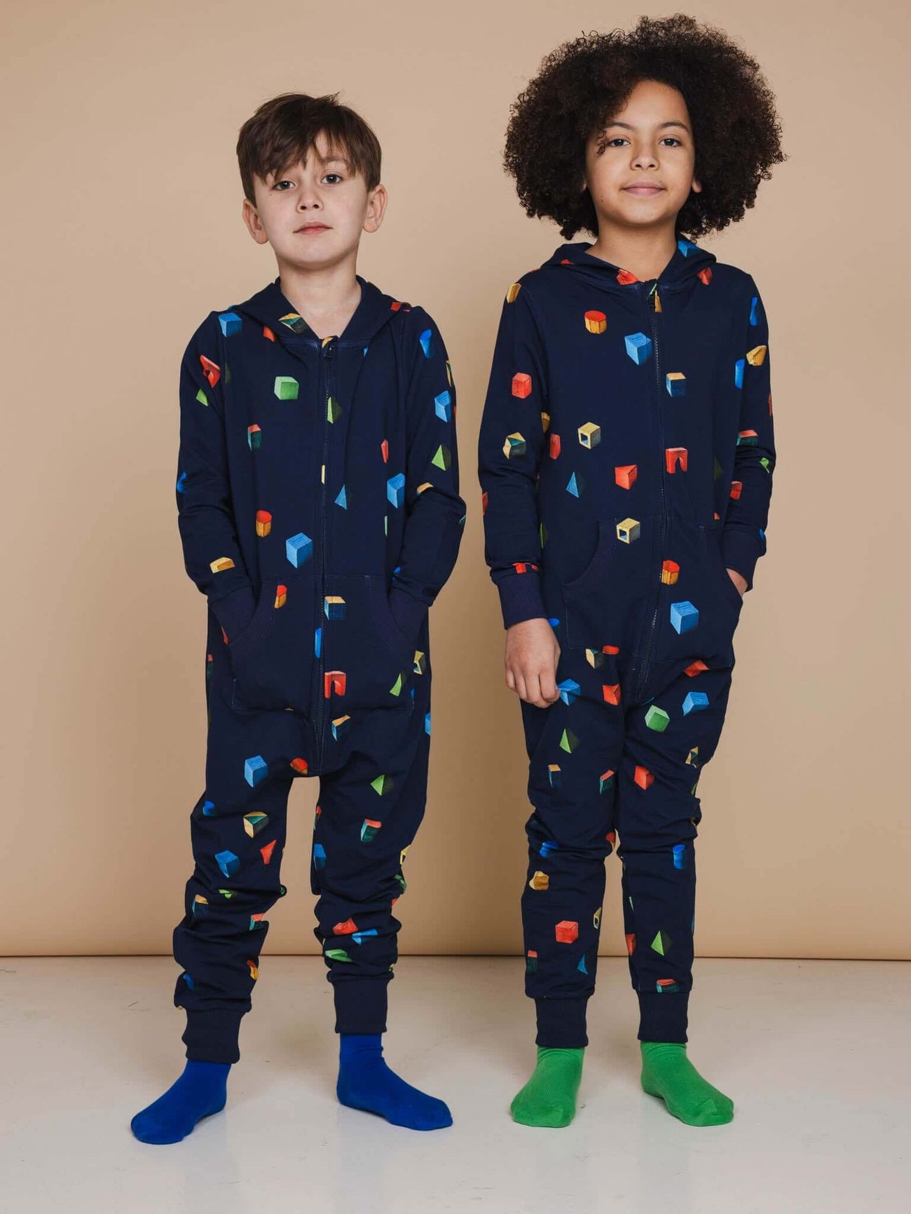 Kinderen in SNURK Building Blocks Onesie Kids met kleurrijke blokken op donkerblauwe achtergrond.