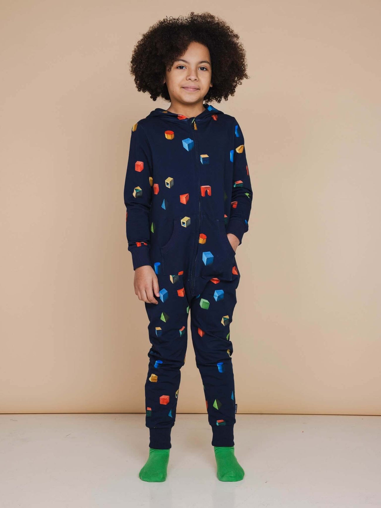 Kind in SNURK Building Blocks Onesie Kids met kleurrijke blokken op een donkerblauwe achtergrond.