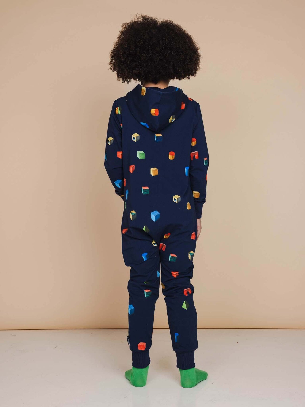 A child wearing the SNURK Building Blocks Onesie Kids, featuring a colorful building blocks print on a dark blue background.