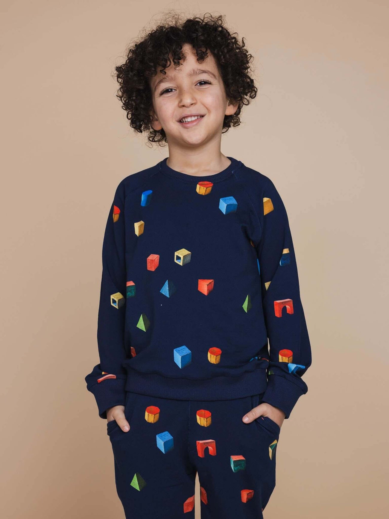Een jongen draagt de SNURK Building Blocks Sweater Kids met kleurrijke blokken op een donkerblauwe achtergrond.
