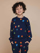 Een jongen draagt de SNURK Building Blocks Sweater Kids met kleurrijke blokken op een donkerblauwe achtergrond.
