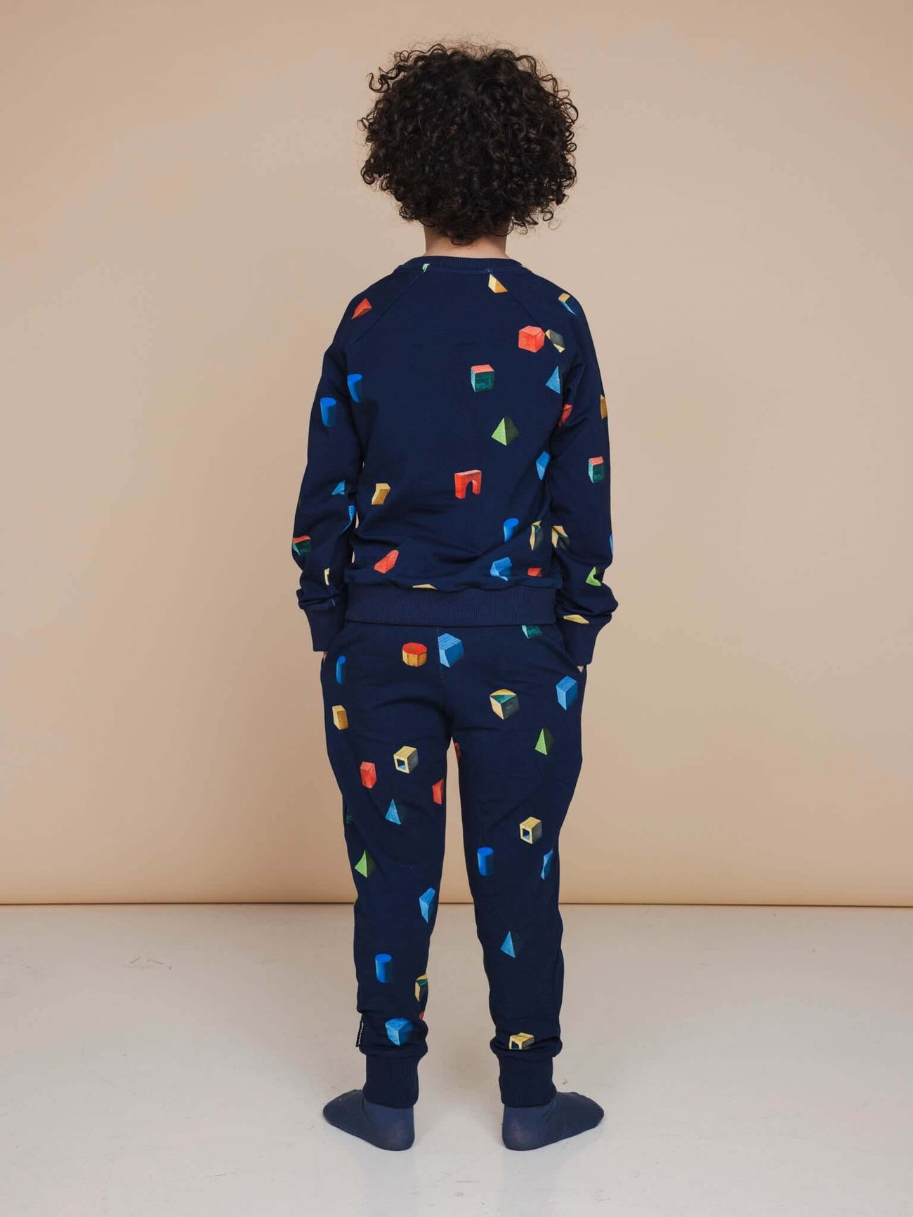 A child wearing the SNURK Building Blocks Sweater Kids, featuring a colorful block print on a dark blue background.