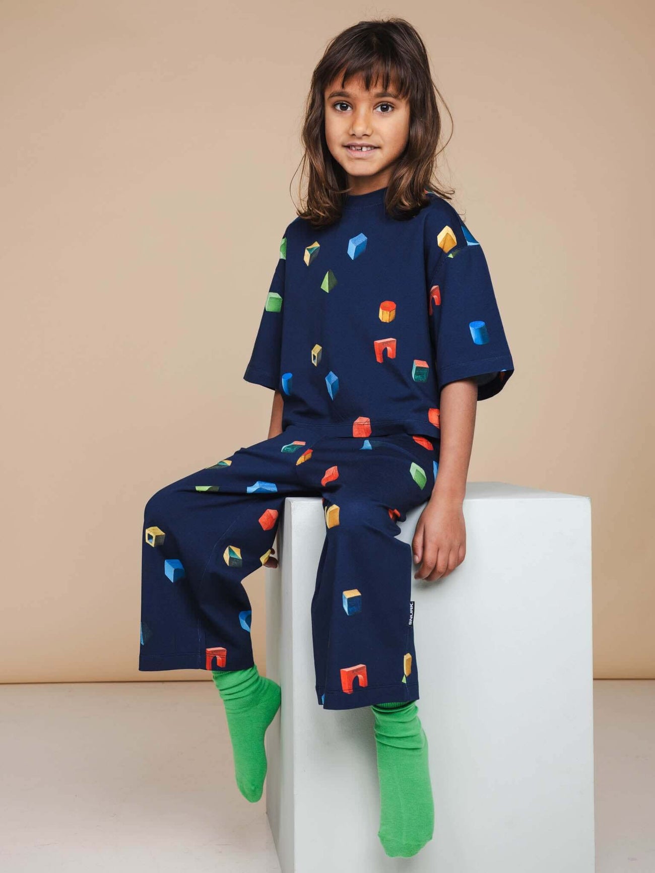 SNURK Building Blocks Wijde broek Kids - Kind in kleurrijke broek met blokkenprint op donkerblauwe achtergrond.