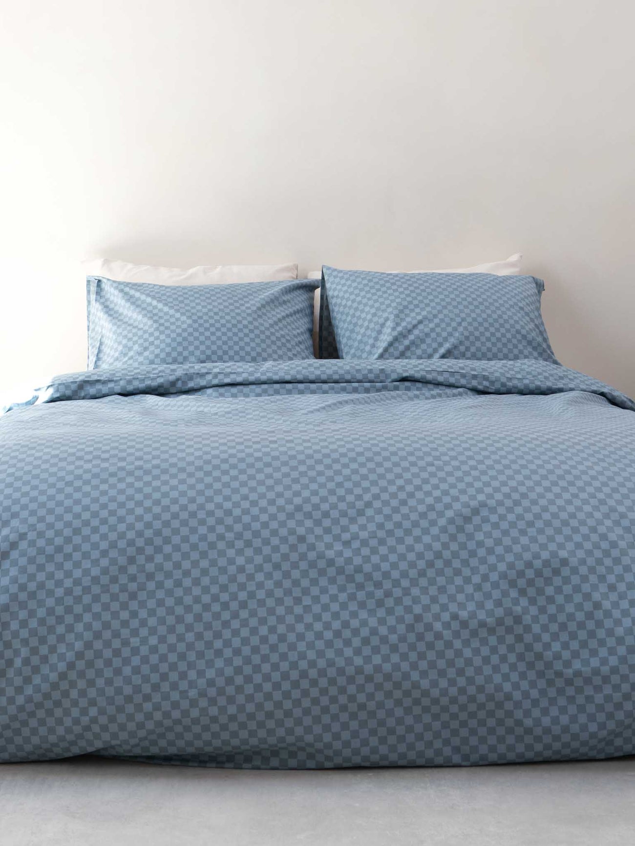 SNURK Check Faded Blue dekbedovertrek op een bed met kussens, gemaakt van 100% biologisch katoen voor slaapcomfort.