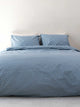 SNURK Check Faded Blue dekbedovertrek op een bed met kussens, gemaakt van 100% biologisch katoen voor slaapcomfort.