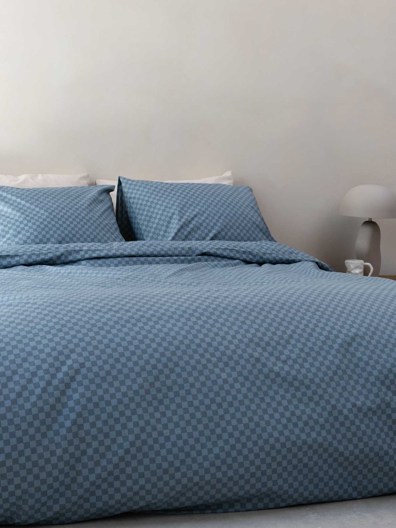 SNURK Check Faded Blue dekbedovertrek op bed met kussens in een blauwe geruite stijl, perfect voor elke slaapkamer.