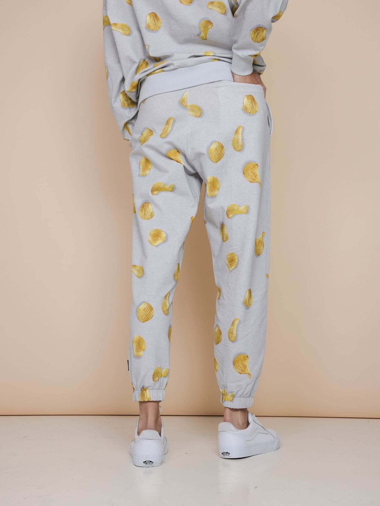 SNURK Chips Broek Relaxed Unisex met all-over print van chips op een lichtgrijze achtergrond.
