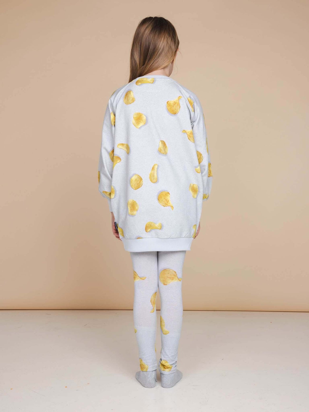 A child wearing SNURK Chips Legging Kids with a grey sweater featuring a chips print.