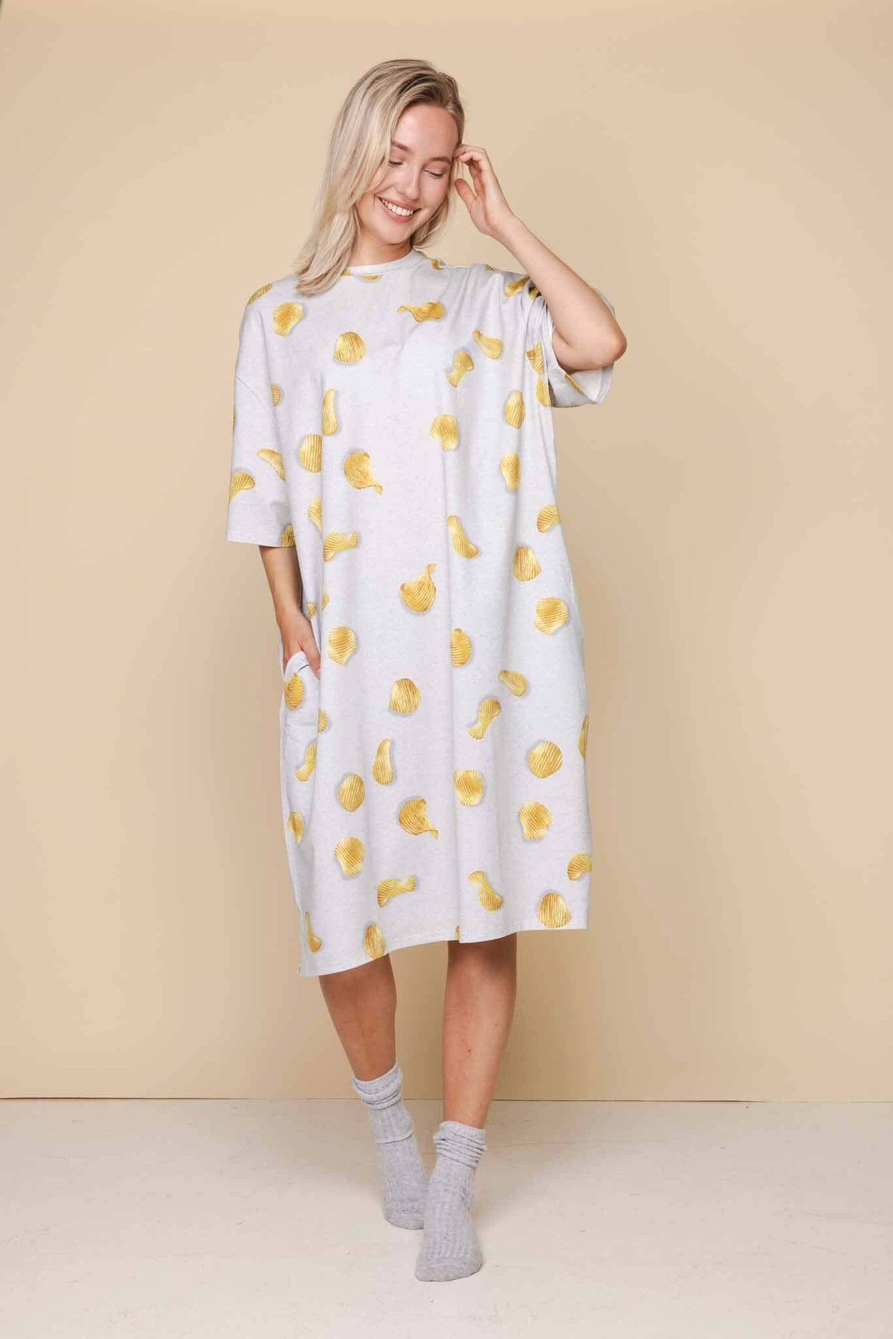 SNURK Chips Relaxed Tee Dress Dames met naturel chips print op een lichtgrijze achtergrond, gedragen door een vrouw.