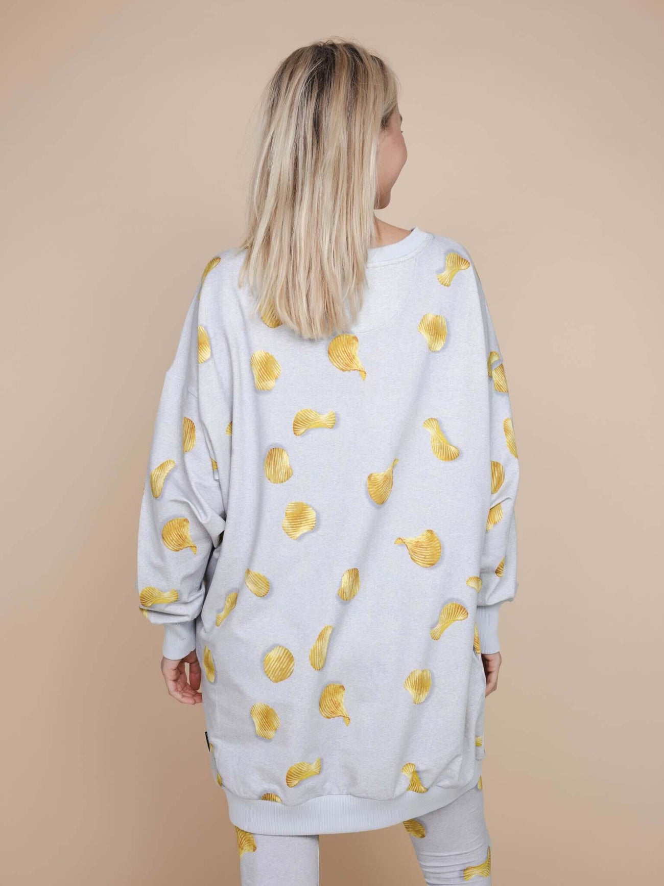 Model wearing the SNURK Chips Sweater Dress Dames with a playful all-over chips print on a light gray background.