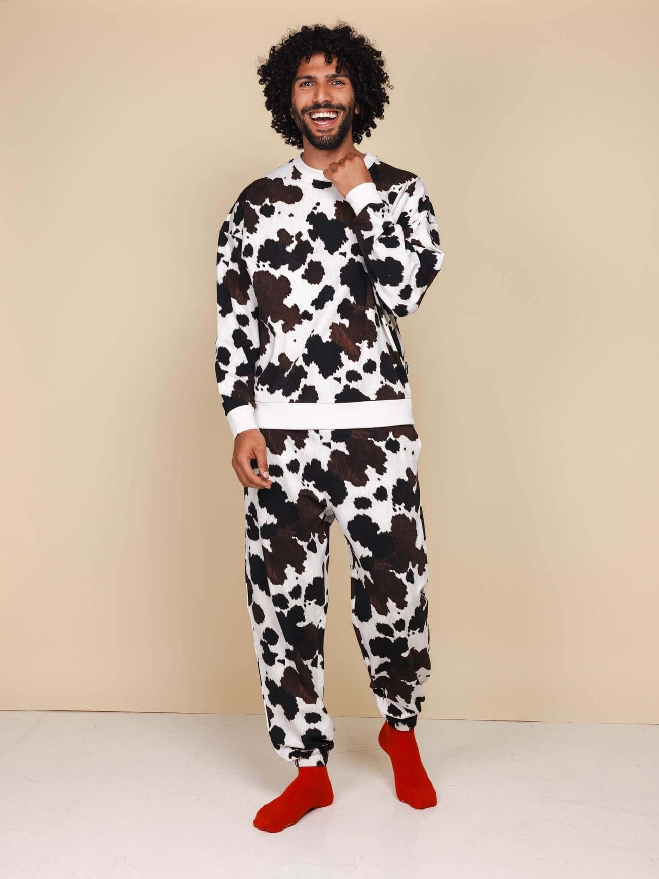 Man in SNURK Cow Sweater Heren met koeienhuidprint en rode sokken, comfortabel en stijlvol.