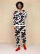 Man in SNURK Cow Sweater Heren met koeienhuidprint en rode sokken, comfortabel en stijlvol.