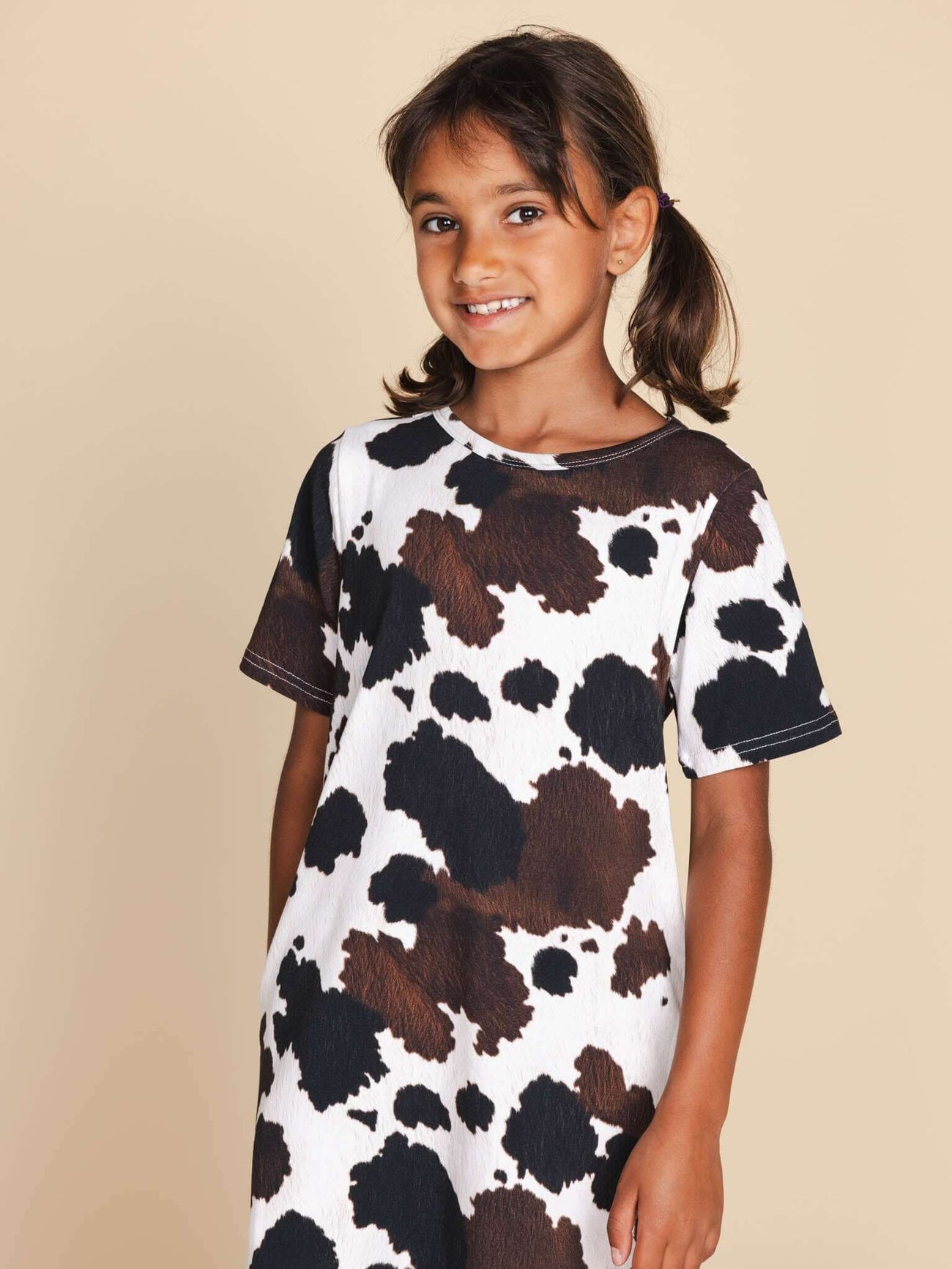 Kind in SNURK Cow T-shirt Dress Kids met stoere koeienprint op een neutrale achtergrond.