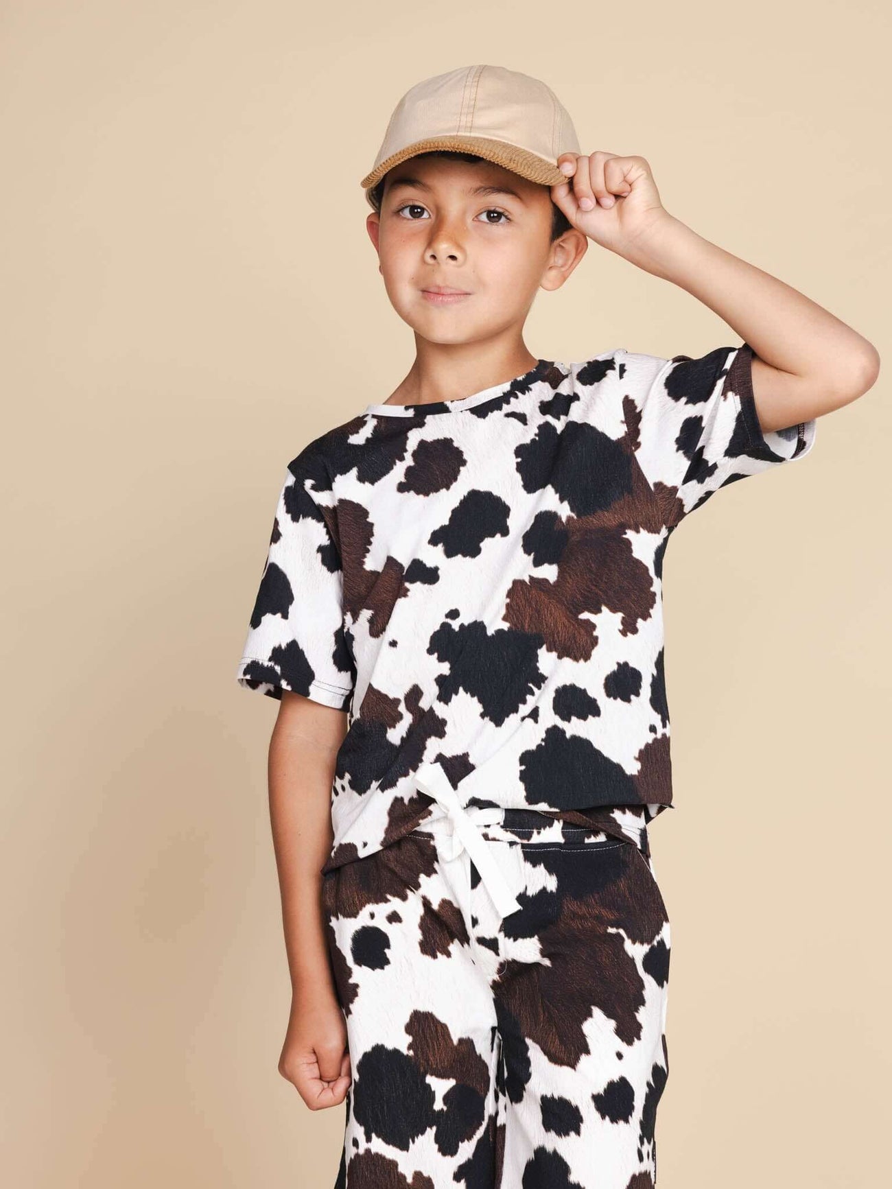 Kind met een pet die het SNURK Cow T-shirt Kids draagt, gekleed in een coole koeienprint.