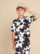 Kind met een pet die het SNURK Cow T-shirt Kids draagt, gekleed in een coole koeienprint.