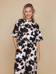 Vrouw in SNURK Cow Wijde Broek Dames met koeienprint, ontspannen pasvorm en diepe zakken.
