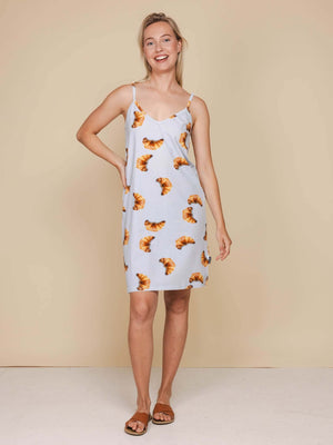 SNURK Croissants Strap Dress Dames model met spaghettibandjes en croissantjesprint in een beige achtergrond.