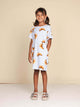 SNURK Croissants T-shirt Dress Kids gedragen door een meisje met een vrolijke uitstraling, gekleed in een jurkje met croissants.
