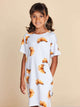 SNURK Croissants T-shirt Dress Kids met schattige croissantjes op een meisje in een casual outfit.