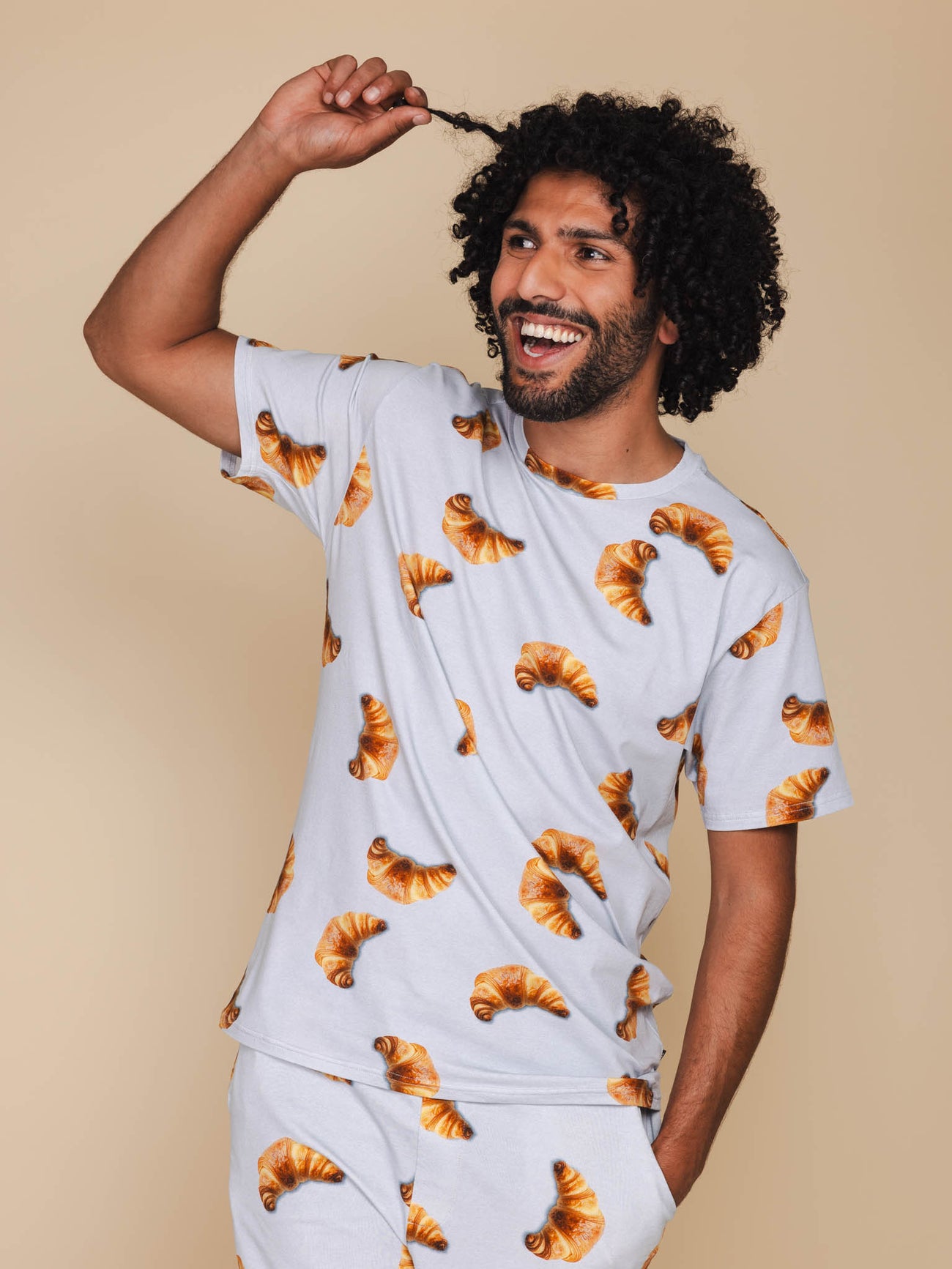 SNURK Croissants T-shirt Unisex met een model in een croissant patroon op een beige achtergrond.