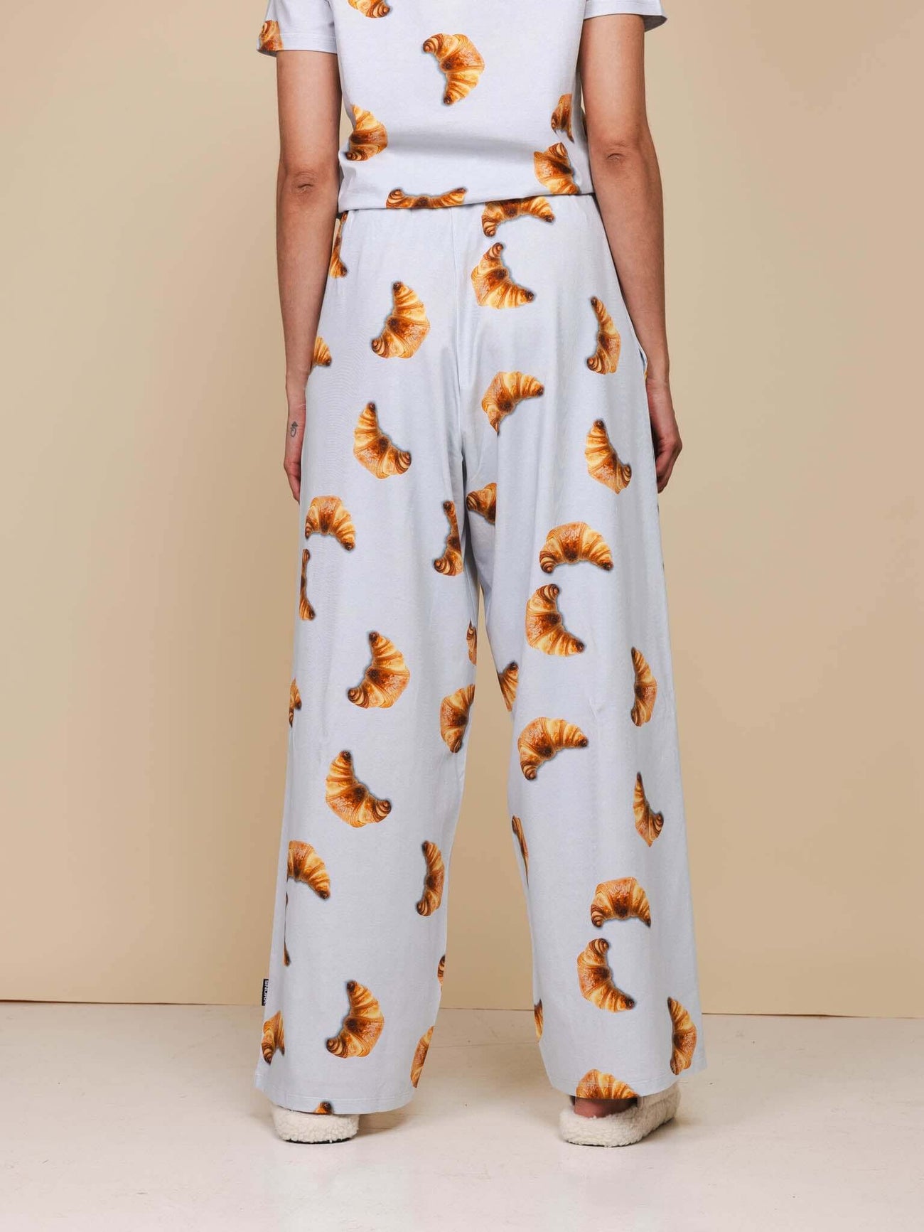 SNURK Croissants Wijde Broek Dames, achteraanzicht van broek met croissantjes op een zachte blauwe achtergrond.