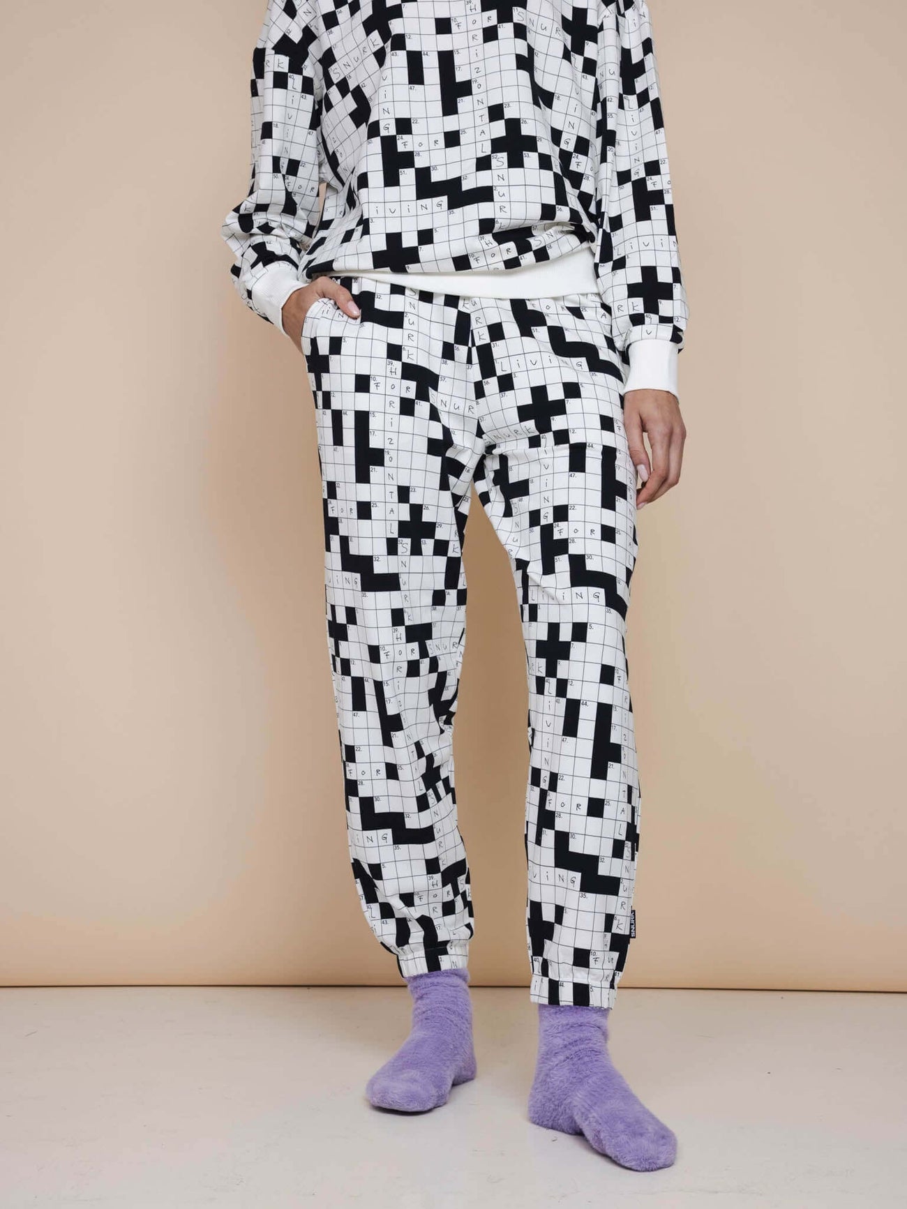 Model draagt SNURK Crossword Broek Relaxed Unisex, zwart-witte kruiswoordprint joggingbroek met zachte biologische katoen.