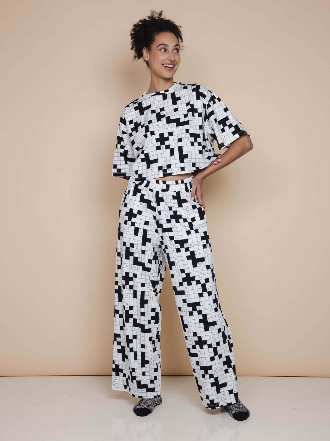 Model met SNURK Crossword Cropped T-shirt Dames en bijpassende broek, zwart-witte puzzelprint.