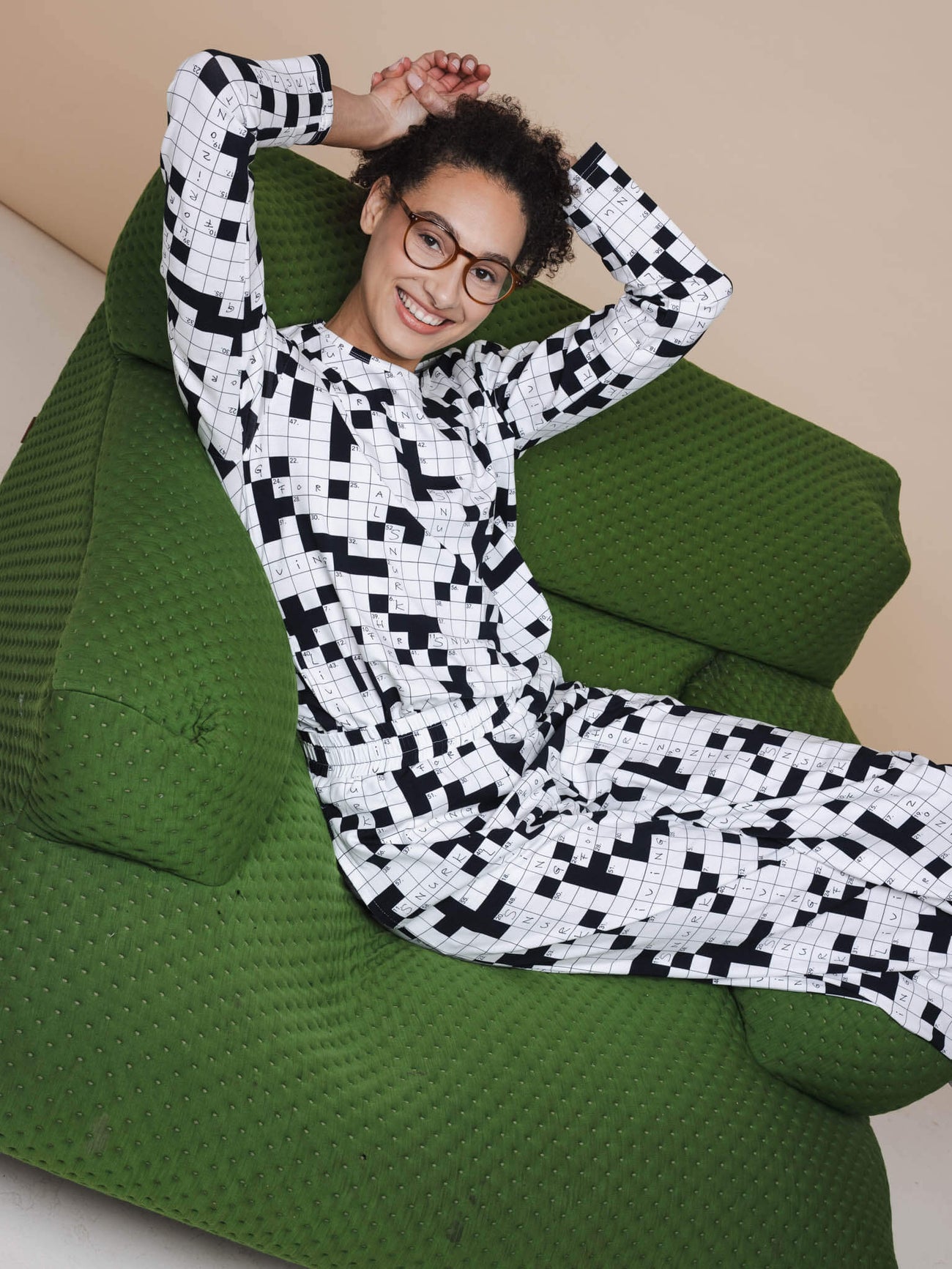 SNURK Crossword Long Sleeve T-shirt Dames op een groene zetel met zwart-wit kruiswoordprint.