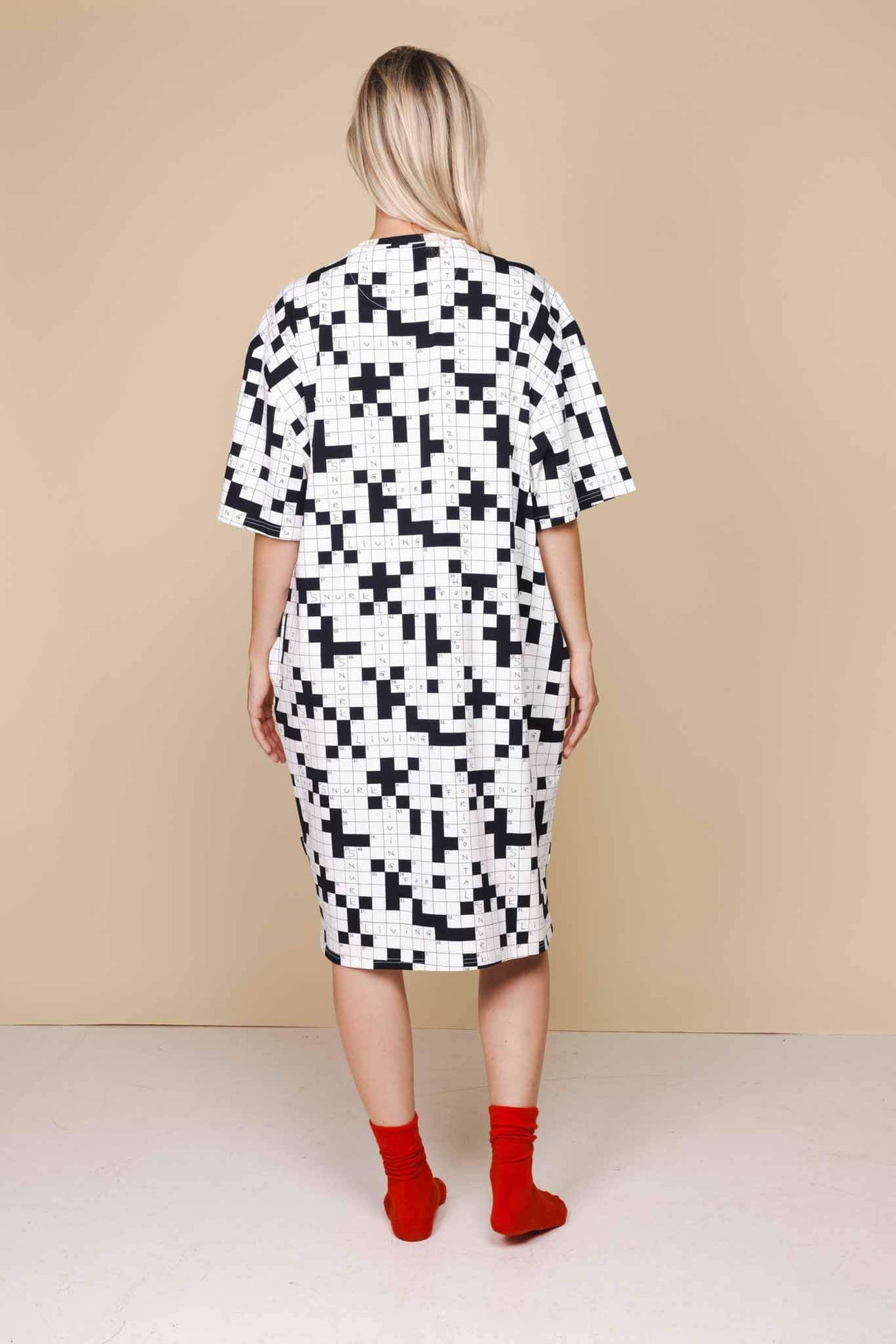 Vrouw in SNURK Crossword Relaxed Tee Dress Dames, oversized jurk met kruiswoordprint en rode sokken.