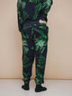 SNURK Dark Forest Broek Relaxed Unisex worn by a person from the back, featuring large dark green leaf print.